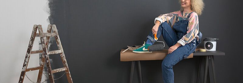 Person sitzt auf einem Tisch und hält eine Farbrolle.